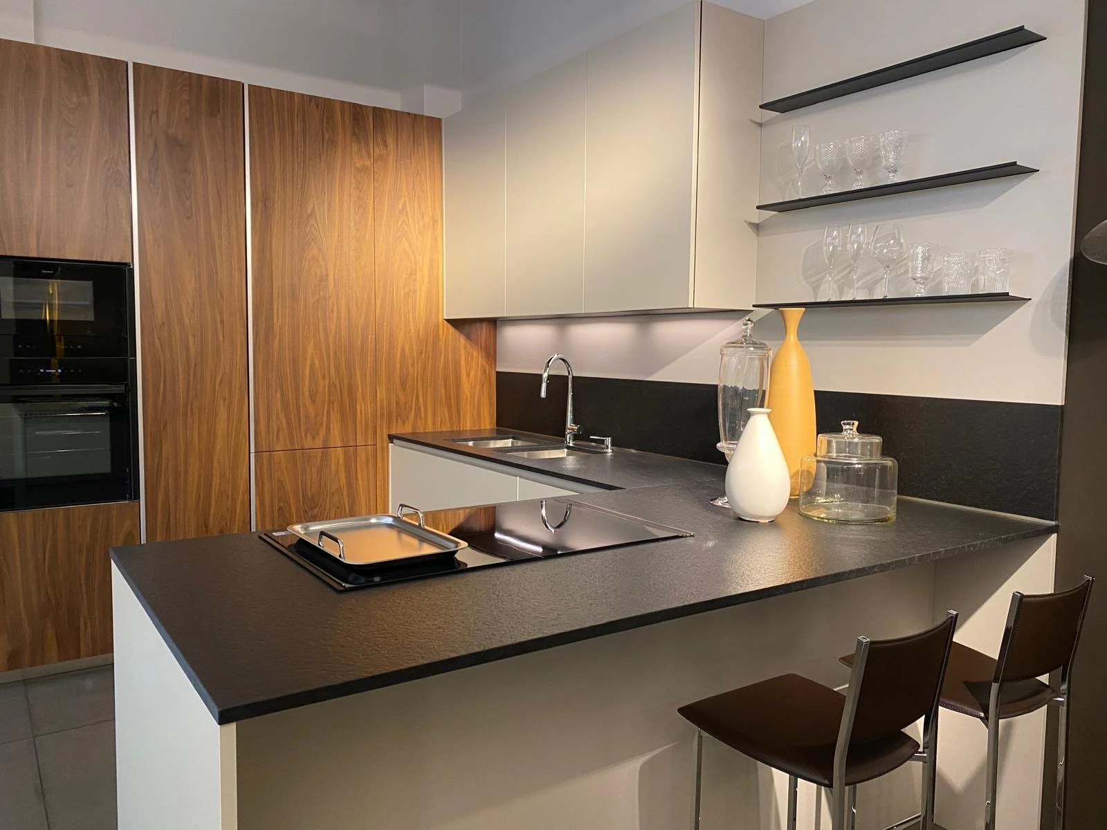 Cucina in showroom con colonne in legno, pensili chiari e piano scuro